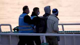 Agentes turcos escoltan a los primeros migrantes deportados bajo una señal de "la seguridad, primero".